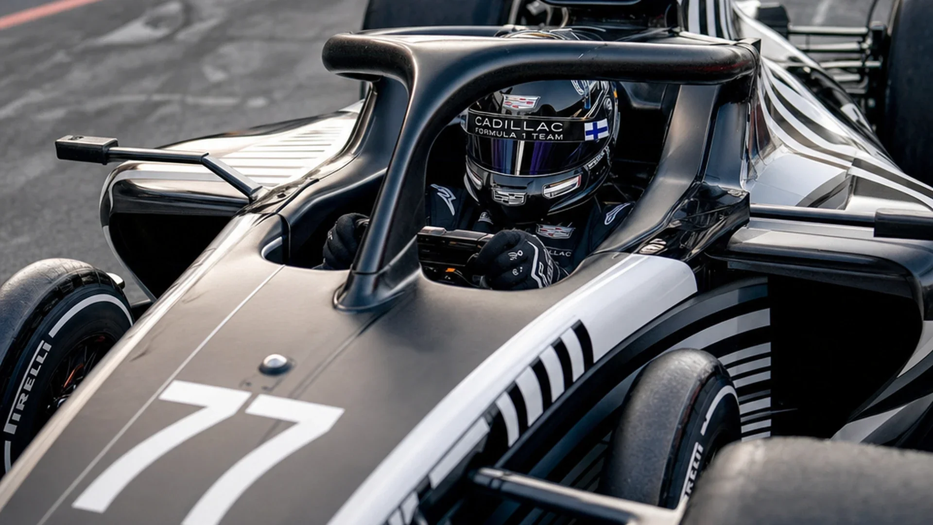 Een coureur met helm en gesloten vizier zit in de cockpit van de Cadillac met nummer 77