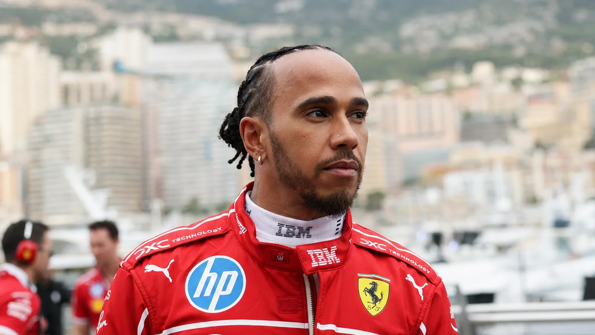 Lewis Hamilton in Ferrari-tenue in de paddock van Monaco, jachthaven op de achtergrond
