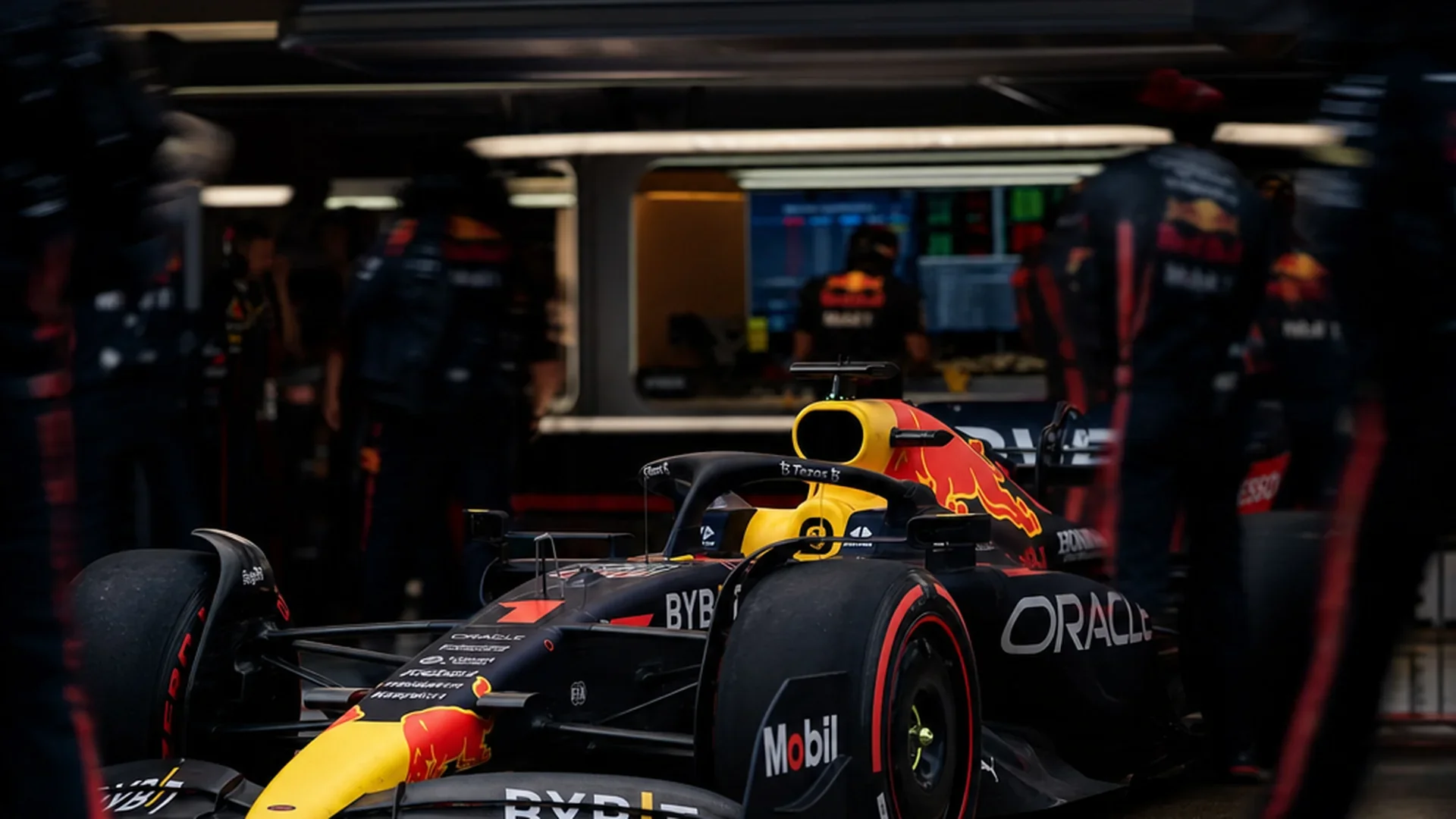 De Red Bull in teamkleuren in de garage, monteurs op de achtergrond